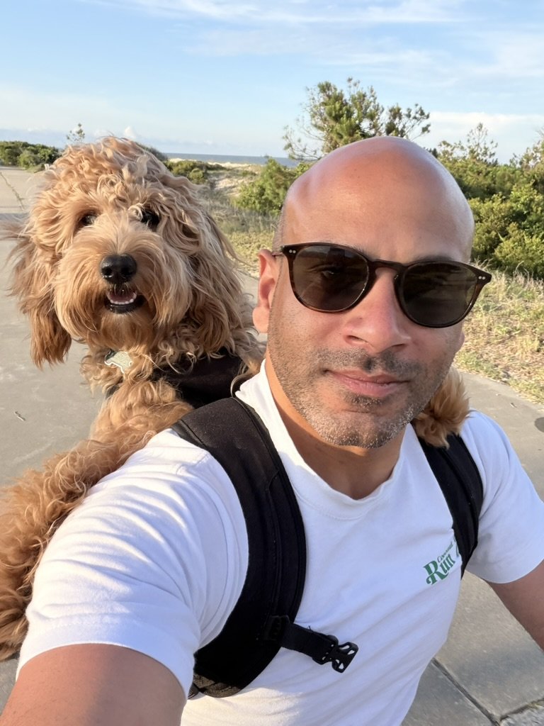 Malek Damiri in sunglasses with Ben the goldendoodle on a coastal trail