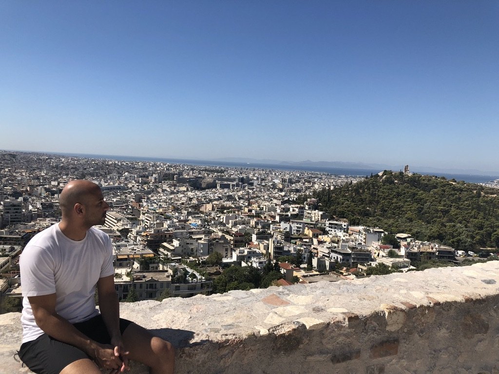 Malek Damiri sitting on a stone wall looking out over Athens, Greece