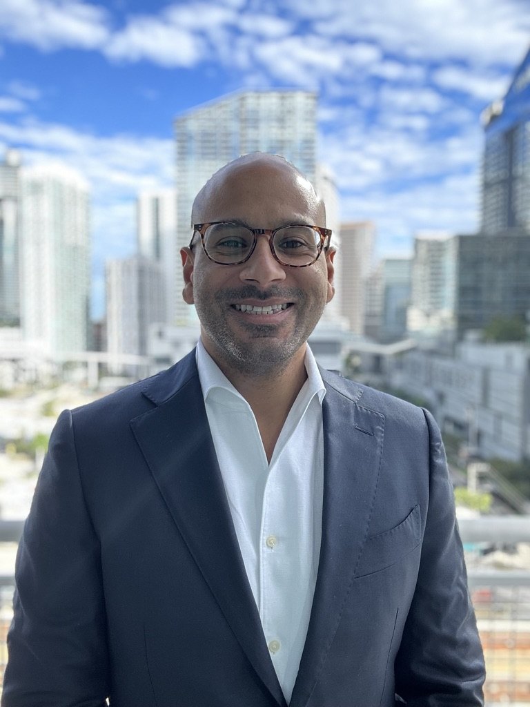 Malek Damiri, Head of Revenue Operations at sFOX, in a navy blazer in front of a city skyline