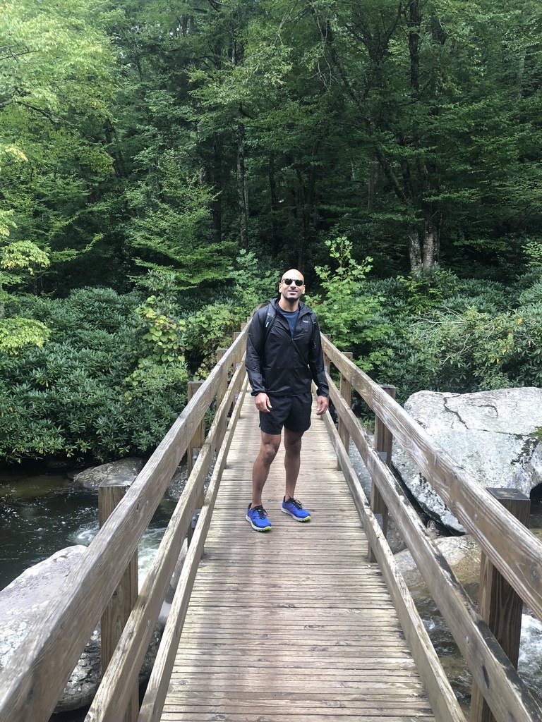 Malek Damiri hiking, standing on a wooden footbridge over a forest stream