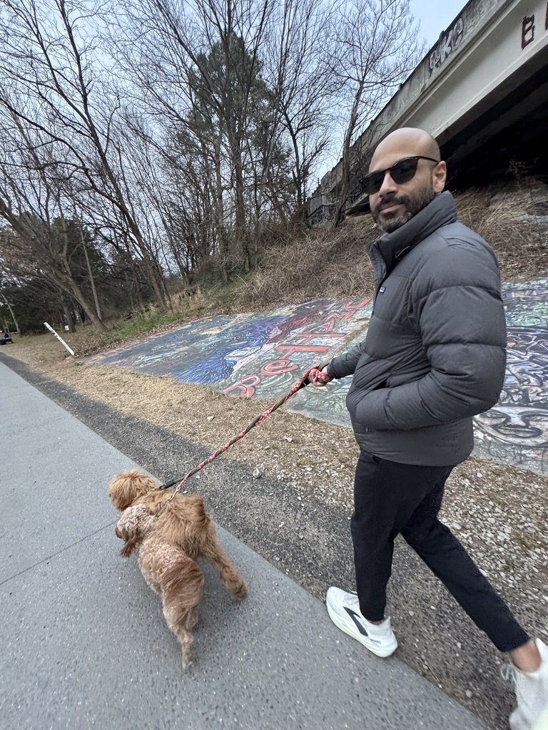 Malek Damiri walking Ben the goldendoodle on a leash along a trail